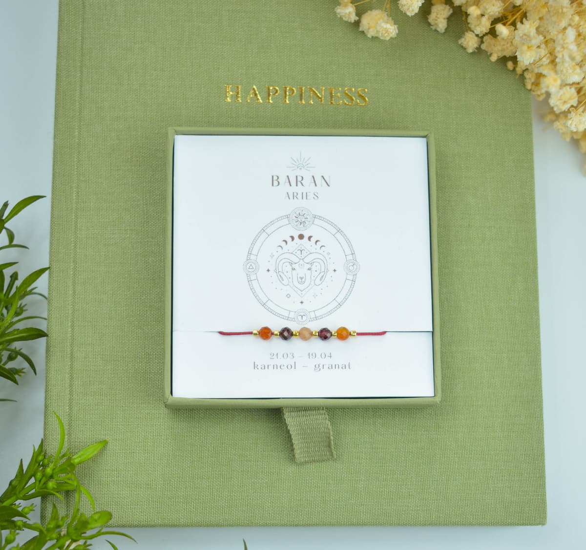 Bransoletka na czerwonym sznurku nylonowym z koralikami z kamieni naturalnych: pomarańczowym karneolem i ciemnoczerwonym granatem. Opakowana w pudełko w kolorze oliwkowym ze złotym logo Happiness.