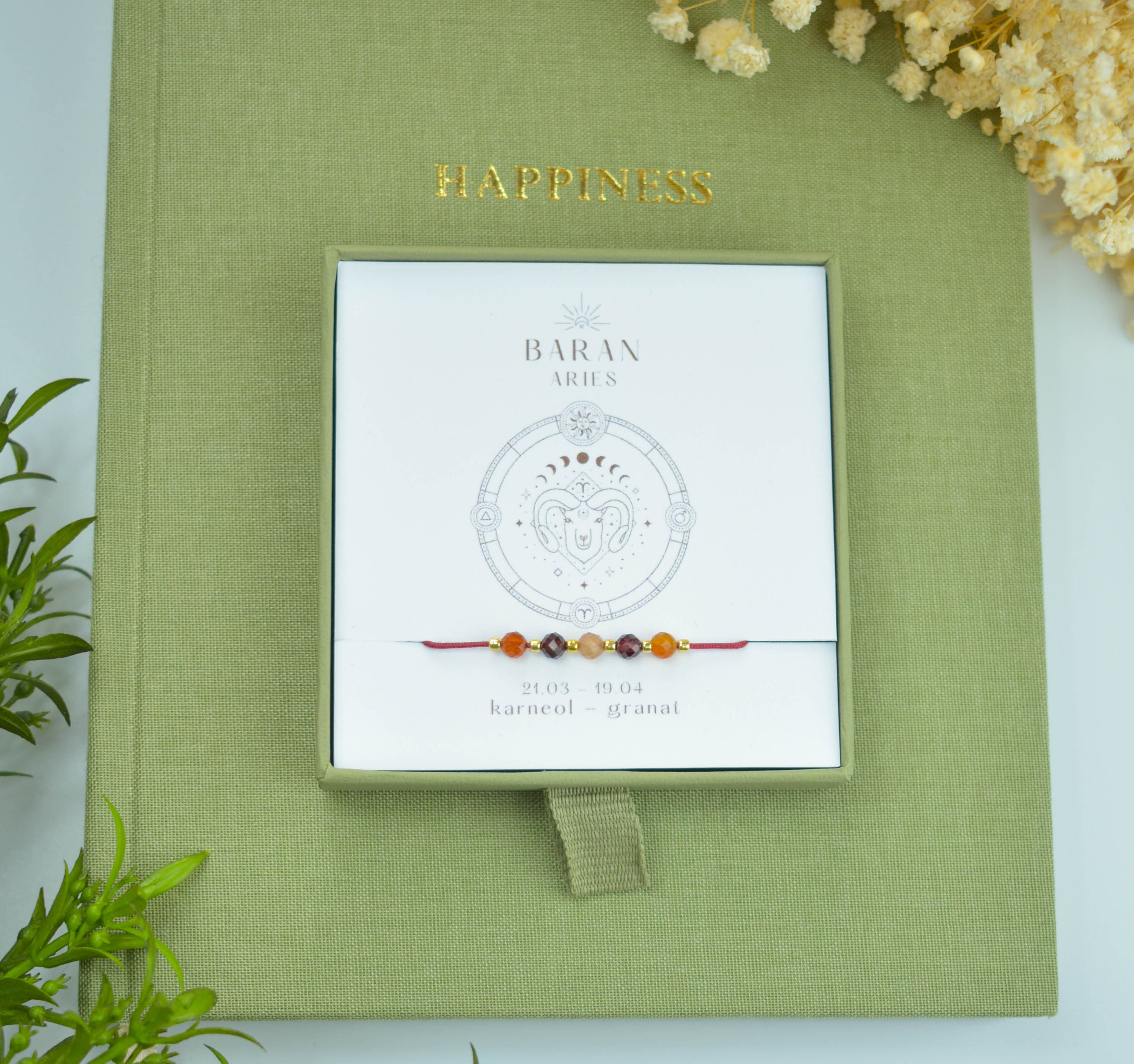 Bransoletka na czerwonym sznurku nylonowym z koralikami z kamieni naturalnych: pomarańczowym karneolem i ciemnoczerwonym granatem. Opakowana w pudełko w kolorze oliwkowym ze złotym logo Happiness.