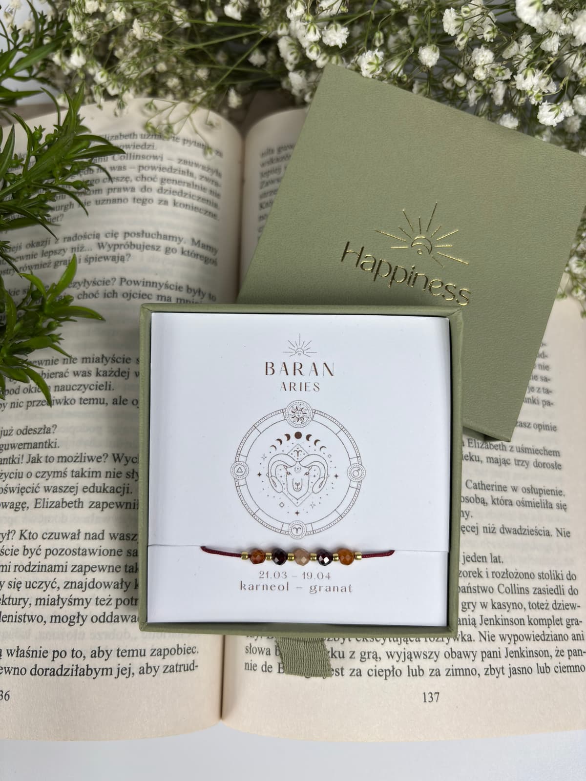 Bransoletka na czerwonym sznurku nylonowym z koralikami z kamieni naturalnych: pomarańczowym karneolem i ciemnoczerwonym granatem. Opakowana w pudełko w kolorze oliwkowym ze złotym logo Happiness.