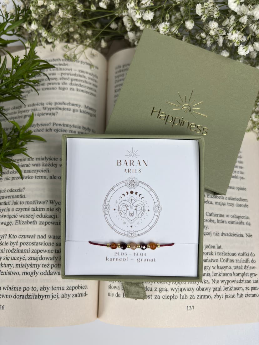 Bransoletka na czerwonym sznurku nylonowym z koralikami z kamieni naturalnych: pomarańczowym karneolem i ciemnoczerwonym granatem. Opakowana w pudełko w kolorze oliwkowym ze złotym logo Happiness.