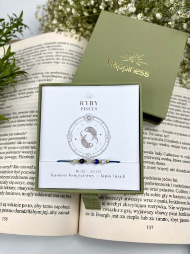 Bransoletka na granatowym sznurku nylonowym z koralikami z kamieni naturalnych: białym kamieniem księżycowym i ciemnoniebieskim lapis lazuri. Opakowana w pudełko w kolorze oliwkowym ze złotym logo Happiness.