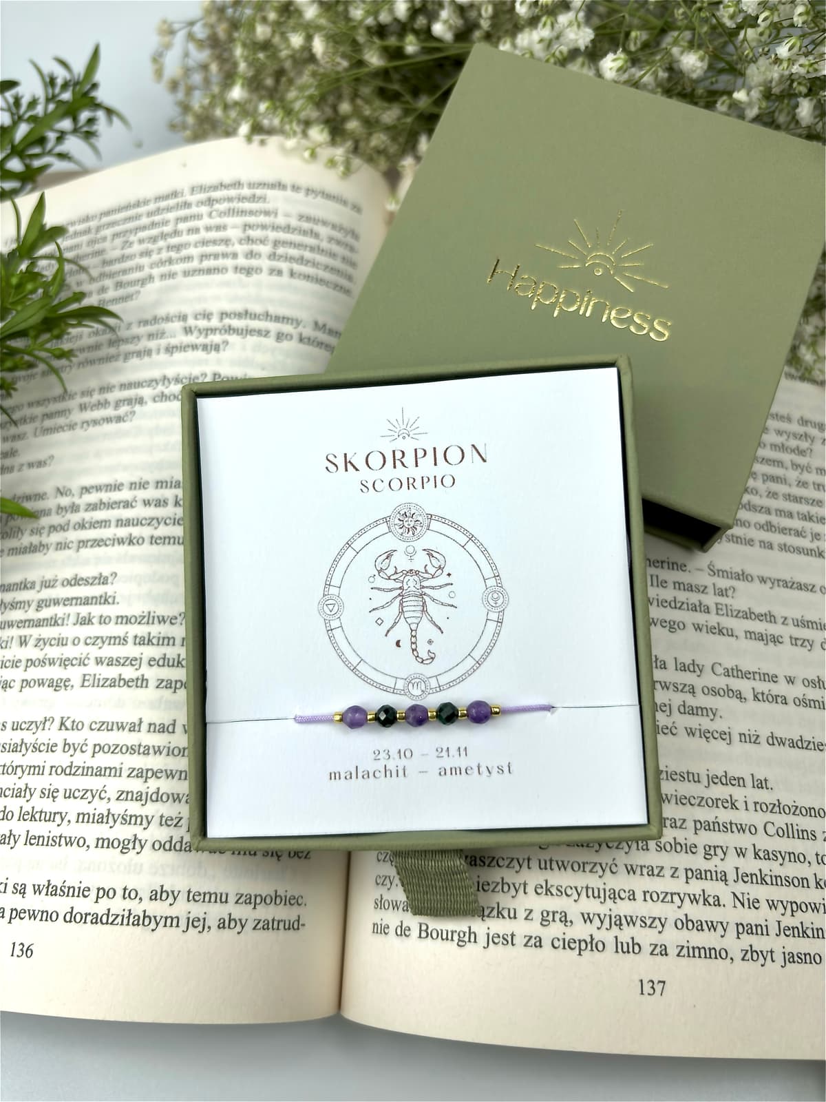 Bransoletka na fioletowym sznurku nylonowym z koralikami z kamieni naturalnych: ciemnozielonym malachitem i fioletowym ametystem. Opakowana w pudełko w kolorze oliwkowym ze złotym logo Happiness.