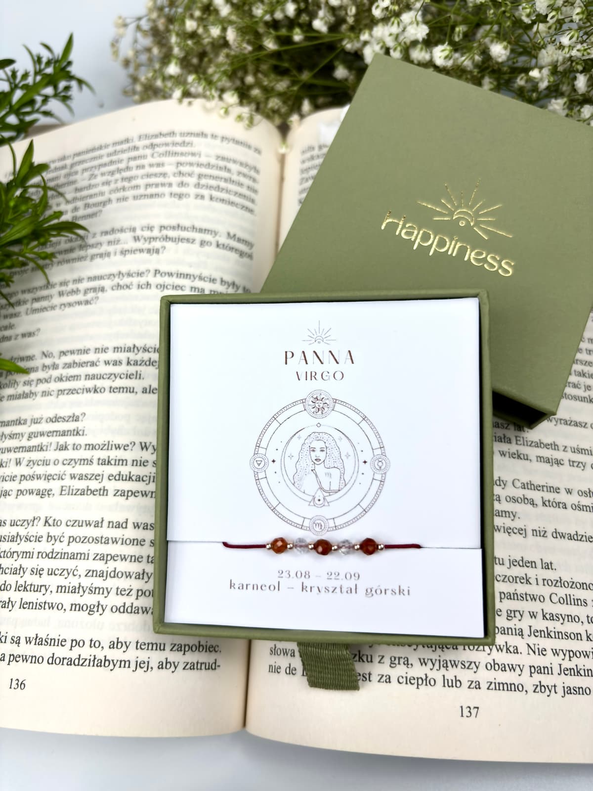 Bransoletka na czerwonym sznurku nylonowym z koralikami z kamieni naturalnych: pomarańczowym karneolem i przezroczystym kryształem górskim. Opakowana w pudełko w kolorze oliwkowym ze złotym logo Happiness.