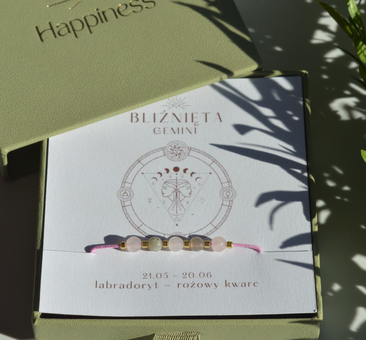 Bransoletka na różowym sznurku nylonowym z koralikami z kamieni naturalnych: szarym labradorytem i różowym kwarcem. Opakowana w pudełko w kolorze oliwkowym ze złotym logo Happiness.