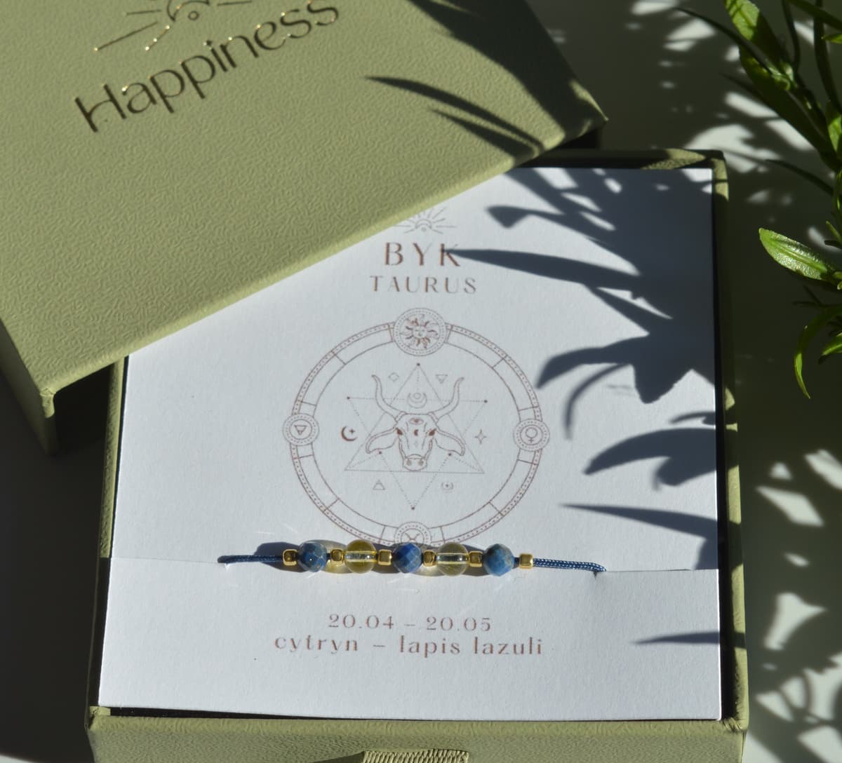 Bransoletka na granatowym sznurku nylonowym z koralikami z kamieni naturalnych: żółtym cytrynem i ciemnoniebieskim lapis lazuri. Opakowana w pudełko w kolorze oliwkowym ze złotym logo Happiness.