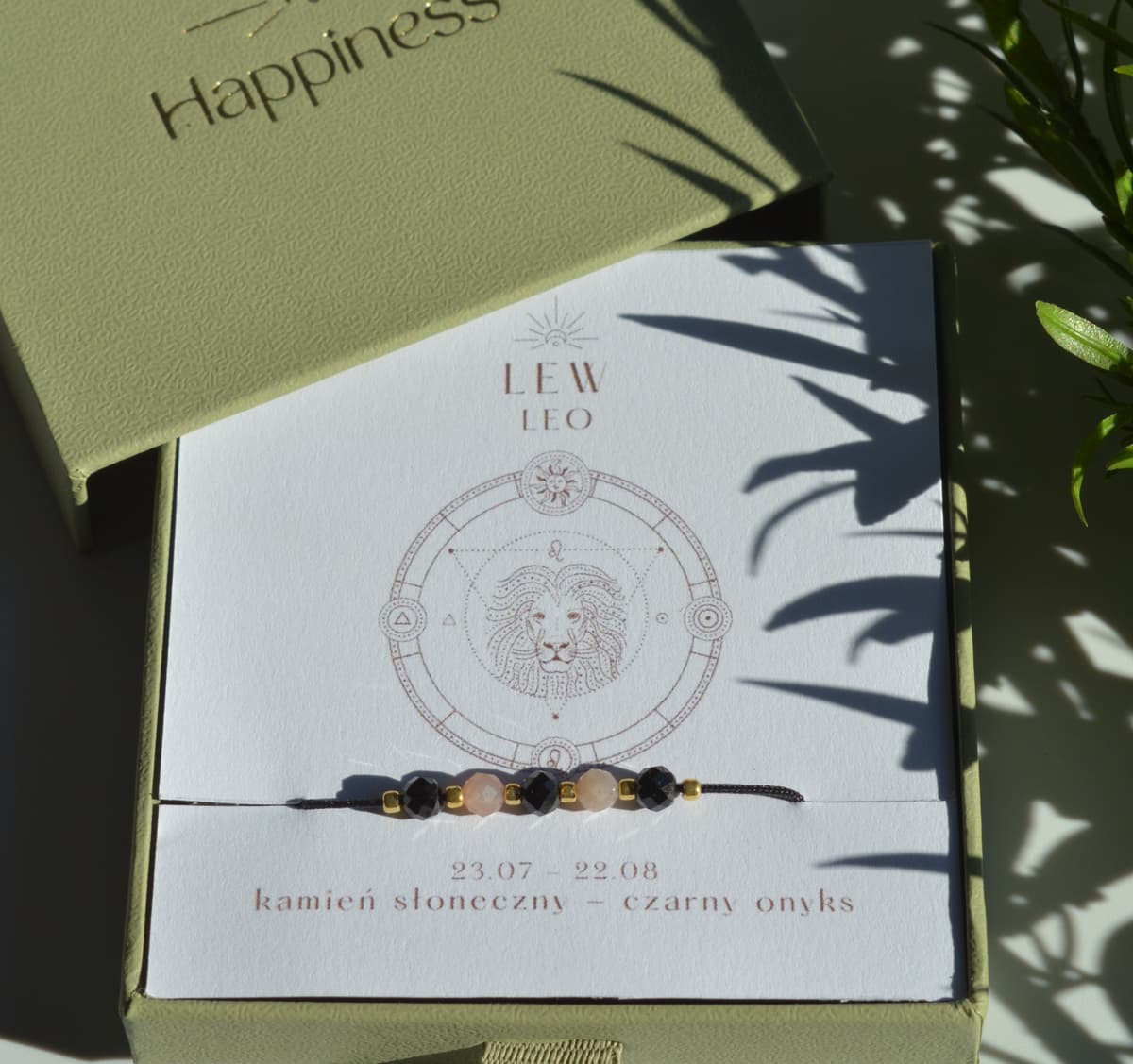 Bransoletka na czarnym sznurku nylonowym z koralikami z kamieni naturalnych: beżowym kamieniem słonecznym i czarnym onyksem. Opakowana w pudełko w kolorze oliwkowym ze złotym logo Happiness.