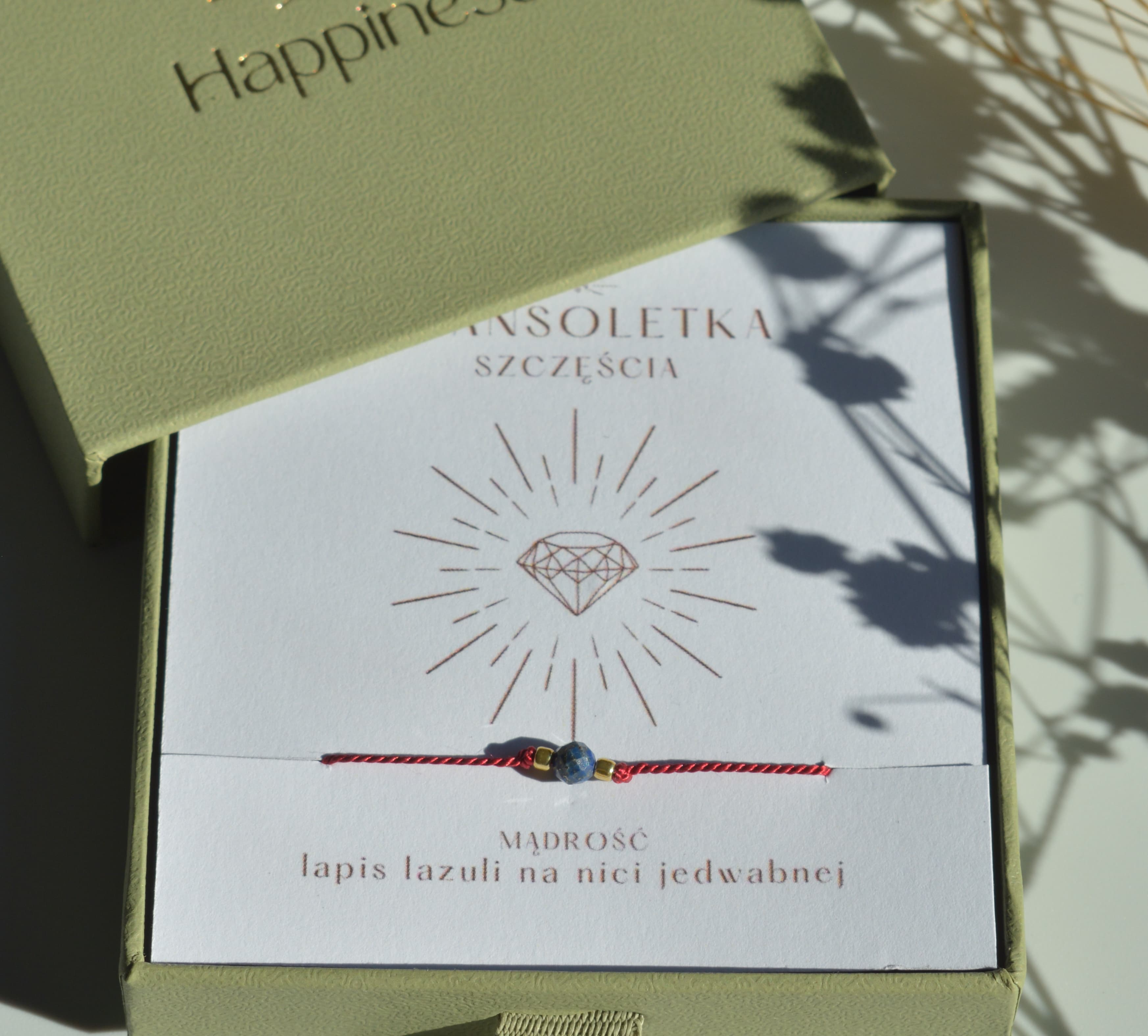Bransoletka szczęścia na ciemnoczerwonej nici jedwabnej. W centralnej części koralik lapis lazuli i dwa malutkie szklane koraliki w kolorze złotym. Opakowana w oliwkowe pudełko ze złotym logo happiness.