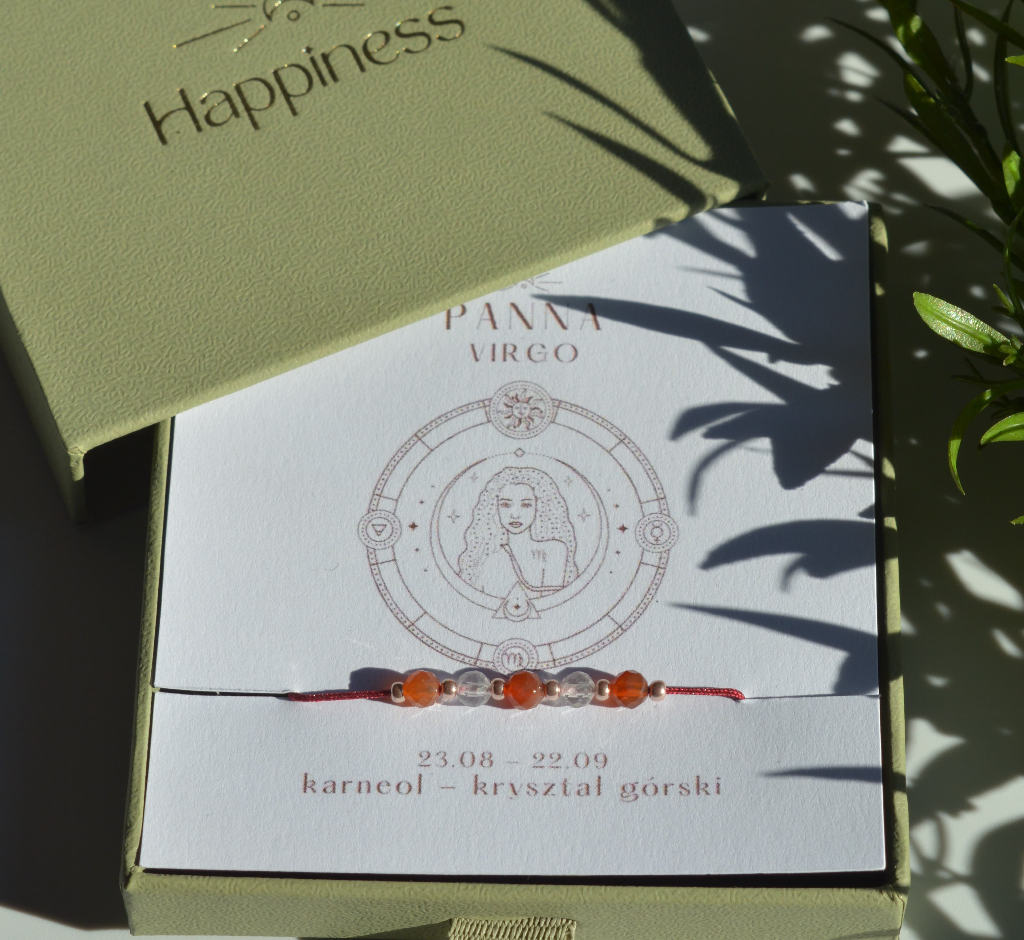 Bransoletka na czerwonym sznurku nylonowym z koralikami z kamieni naturalnych: pomarańczowym karneolem i przezroczystym kryształem górskim. Opakowana w pudełko w kolorze oliwkowym ze złotym logo Happiness.