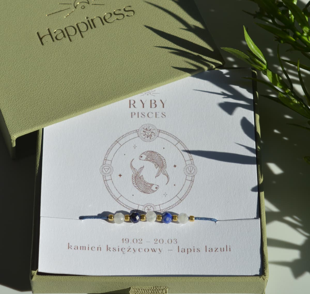 Bransoletka na granatowym sznurku nylonowym z koralikami z kamieni naturalnych: białym kamieniem księżycowym i ciemnoniebieskim lapis lazuri. Opakowana w pudełko w kolorze oliwkowym ze złotym logo Happiness.