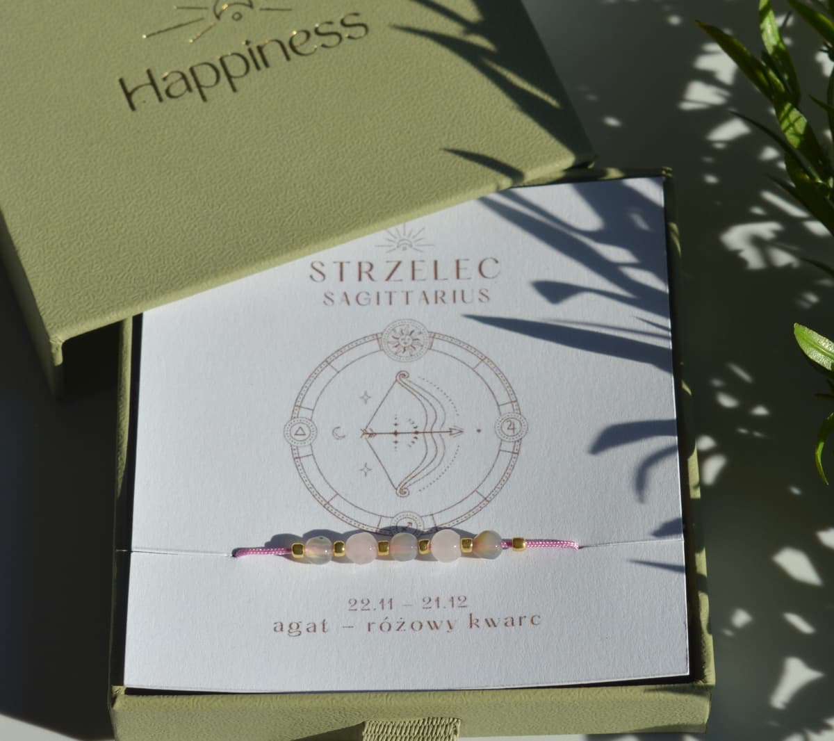 Bransoletka na różowym sznurku nylonowym z koralikami z kamieni naturalnych: szarym agatem i różowym kwarcem. Opakowana w pudełko w kolorze oliwkowym ze złotym logo Happiness.