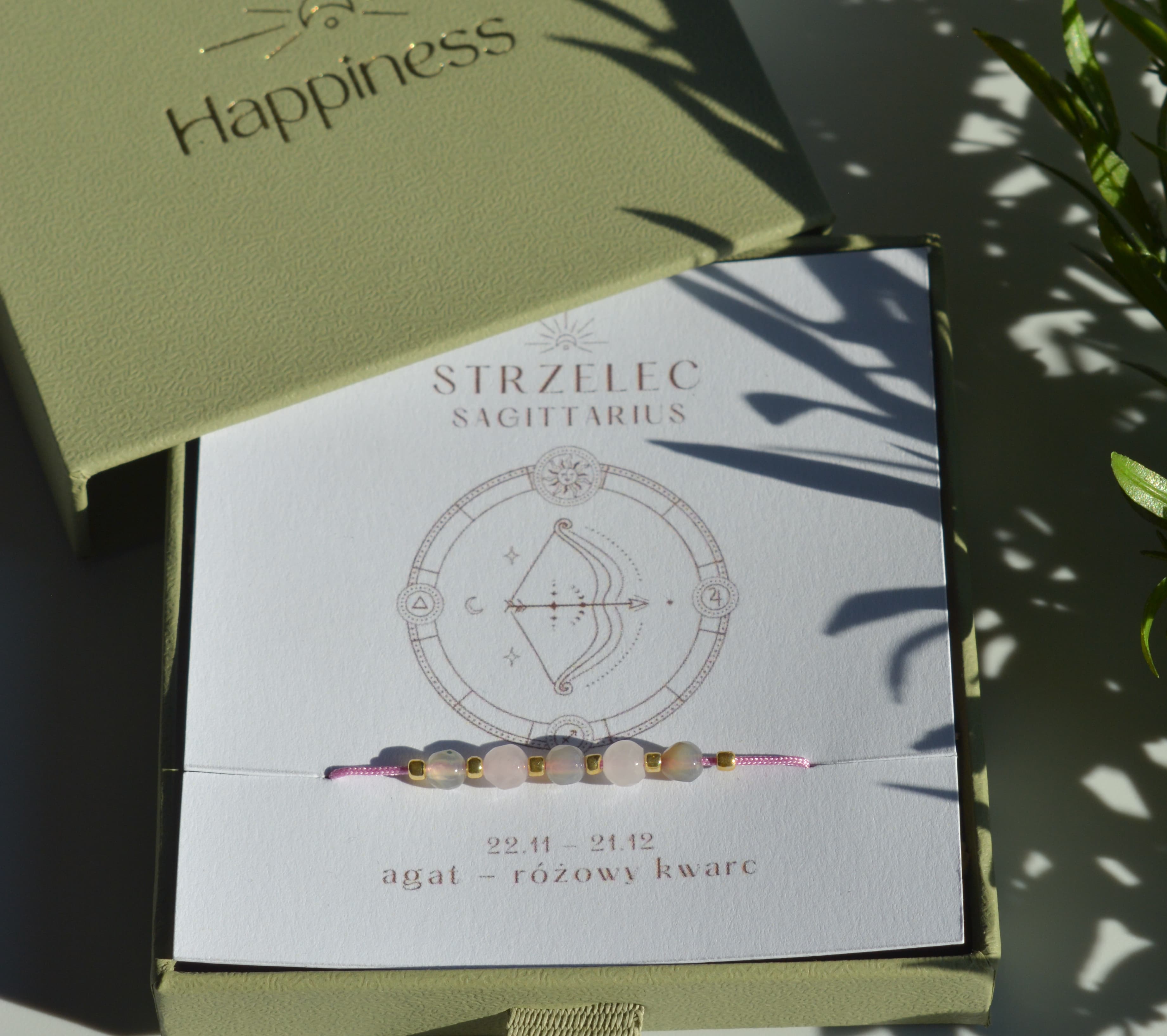 Bransoletka na różowym sznurku nylonowym z koralikami z kamieni naturalnych: szarym agatem i różowym kwarcem. Opakowana w pudełko w kolorze oliwkowym ze złotym logo Happiness.