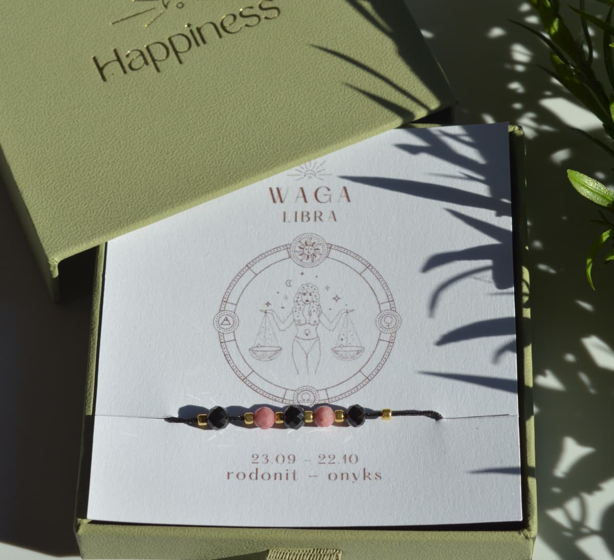 Bransoletka na czarnym sznurku nylonowym z koralikami z kamieni naturalnych: różowym rodonitem i czarnym onyksem. Opakowana w pudełko w kolorze oliwkowym ze złotym logo Happiness.