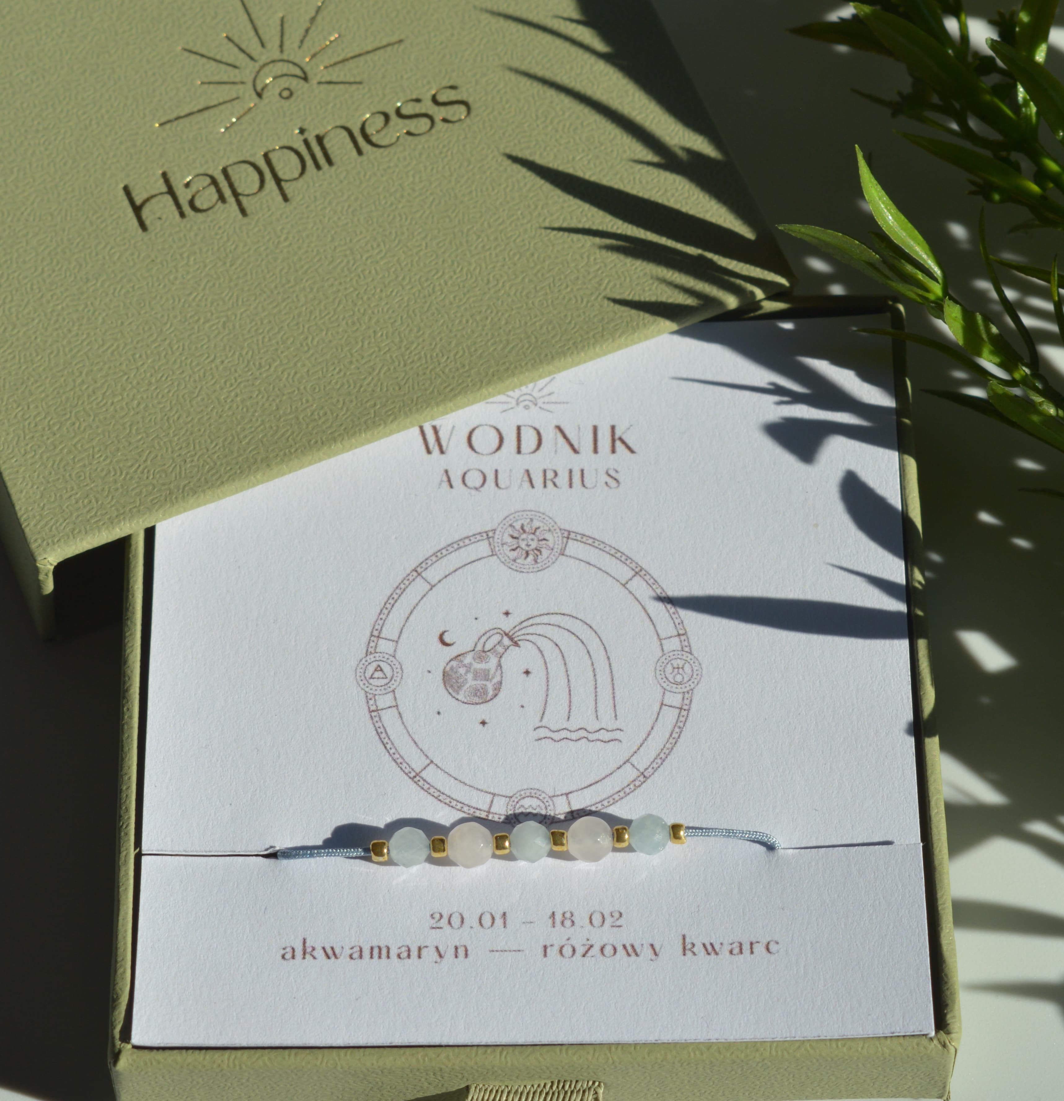 Bransoletka na błękitnym sznurku nylonowym z koralikami z kamieni naturalnych: błękitnym akwamarynem i różowym kwarcem. Opakowana w pudełko w kolorze oliwkowym ze złotym logo Happiness.